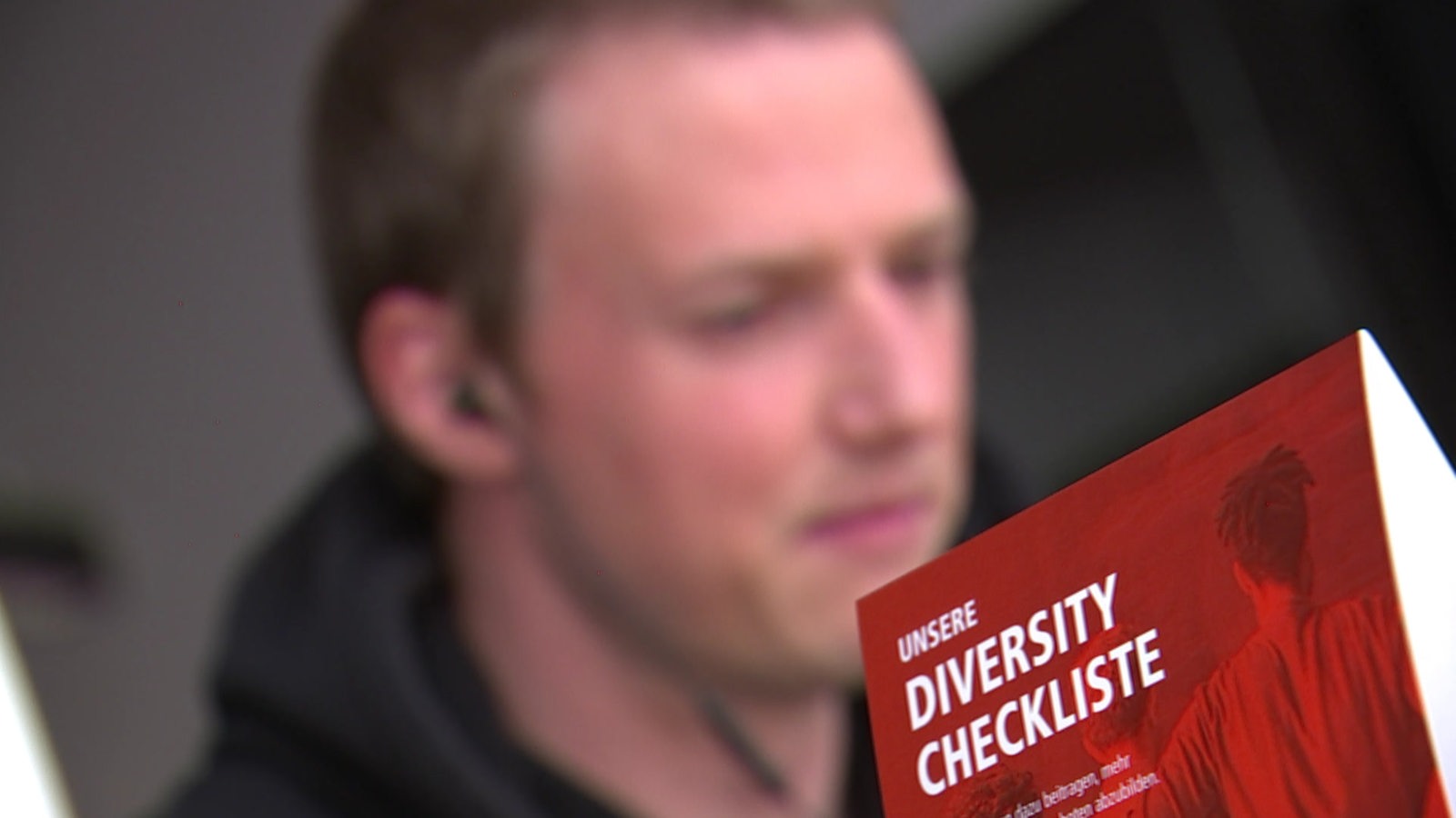 Ein junger Mann liest einen Info-Flyer mit dem Titel "Diversity-Checkliste"