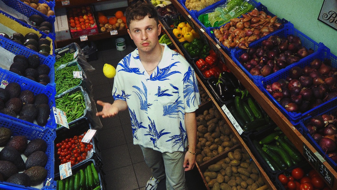 Der Künstler Florida Juicy in einem Supermarkt vor dem Gemüseregal.