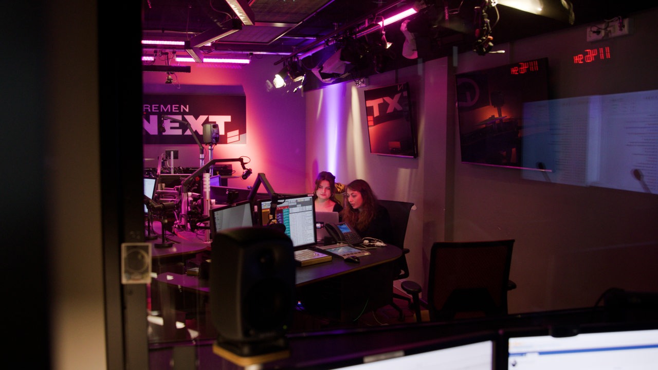 Zwei Frauen sitzen in einem Radiostudio vor dem Mikrofon.