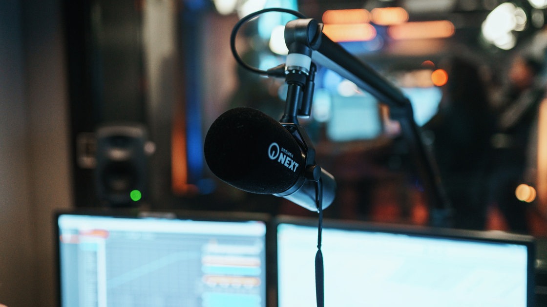 Ein Mikrofon vor zwei Computerbildschirmen in einem Radio-Studio