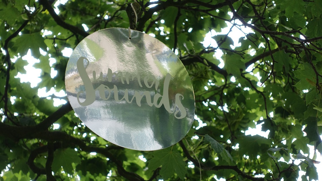 Schild "SummerSounds" mit Aufschrift zwischen grünen Blättern