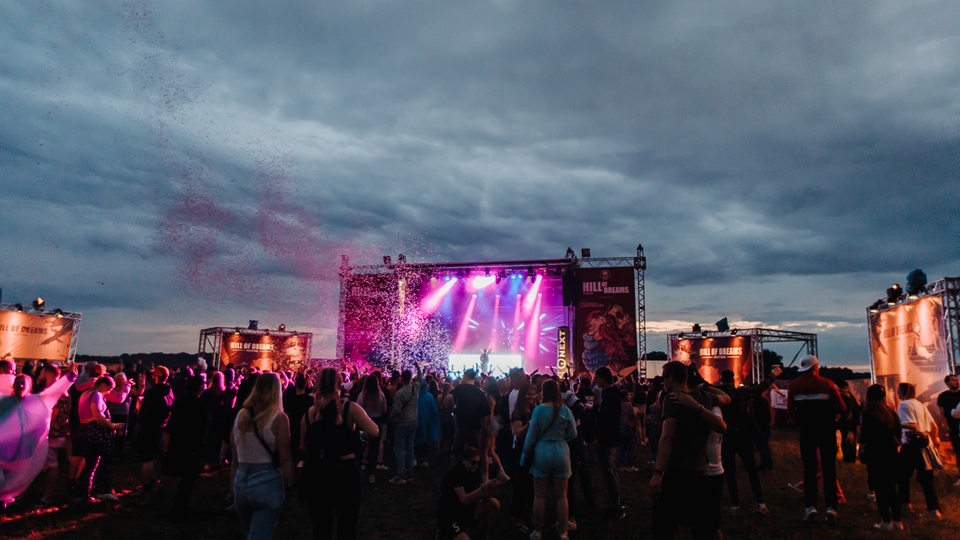 Tanzende Menge auf einem Outdoor-Festival. Im Hintergrund die Hill of Dreams Bühne, sowie Konfetti in der Luft. 